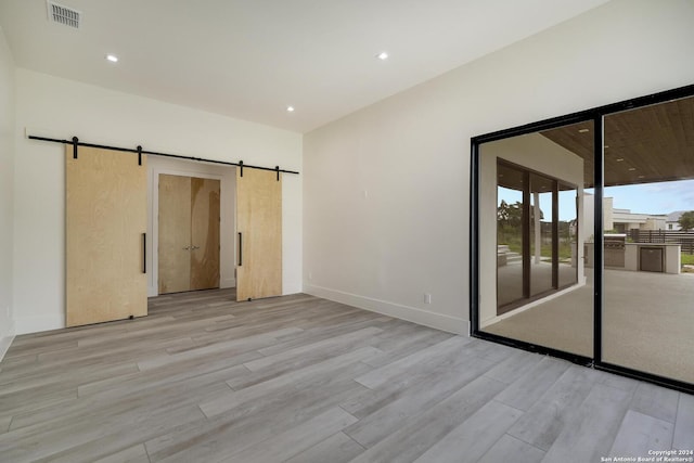 unfurnished room featuring recessed lighting, visible vents, light wood-style flooring, and a barn door