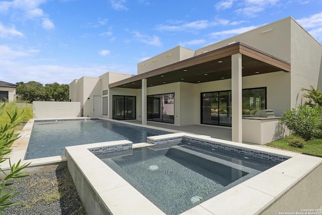 rear view of house featuring an outdoor kitchen, a pool with connected hot tub, a patio, and stucco siding