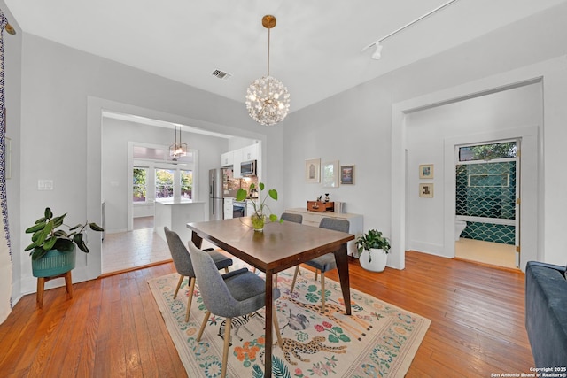 dining space with a chandelier, visible vents, rail lighting, and light wood-style floors