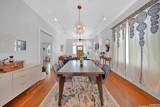 dining room with ceiling fan with notable chandelier, rail lighting, and light wood-style floors