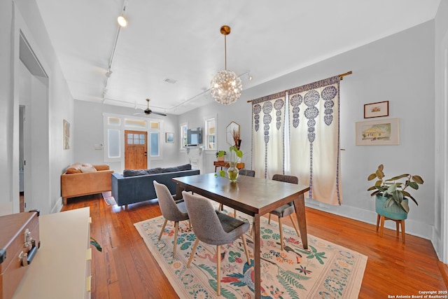 dining area with visible vents, track lighting, ceiling fan with notable chandelier, light wood finished floors, and baseboards