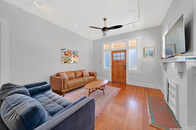 living room featuring a ceiling fan, light wood-style floors, rail lighting, a fireplace, and baseboards