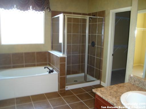 full bathroom with tile patterned flooring, a spacious closet, a shower stall, a garden tub, and vanity