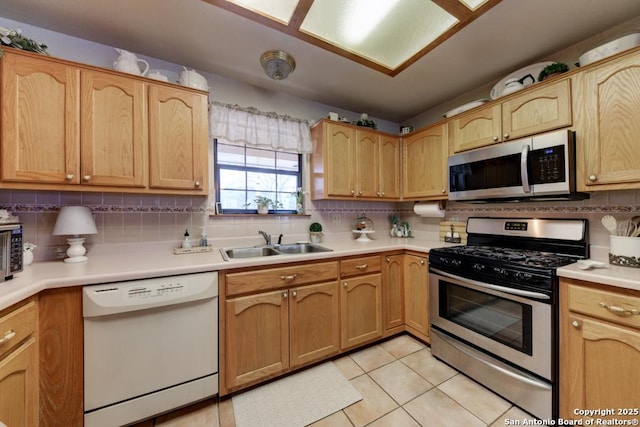 kitchen with a sink, backsplash, appliances with stainless steel finishes, light countertops, and light tile patterned floors