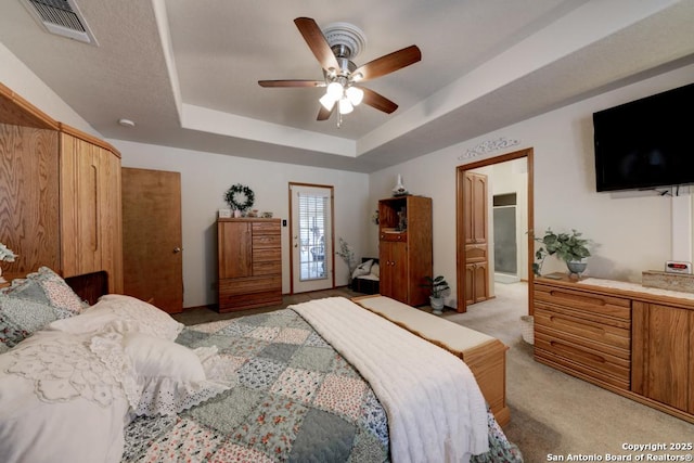 bedroom featuring visible vents, a raised ceiling, light colored carpet, and a ceiling fan