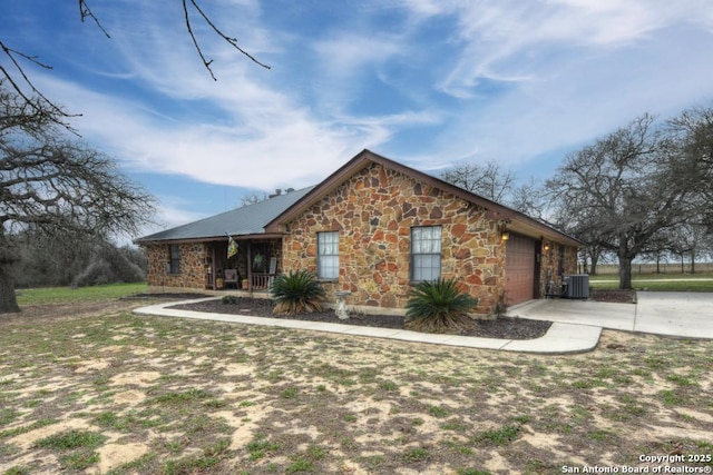 view of front facade with stone siding, a porch, concrete driveway, an attached garage, and central AC unit