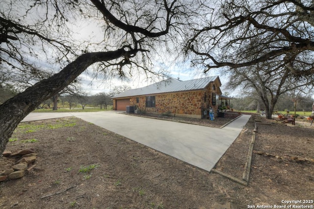 view of property exterior with concrete driveway, cooling unit, metal roof, stone siding, and an attached garage