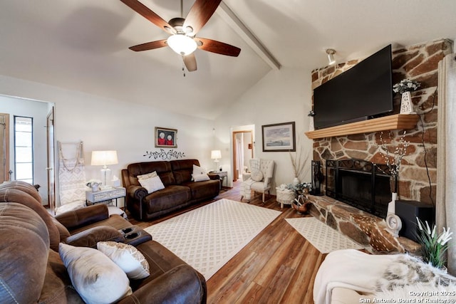 living area featuring lofted ceiling with beams, a stone fireplace, wood finished floors, and a ceiling fan