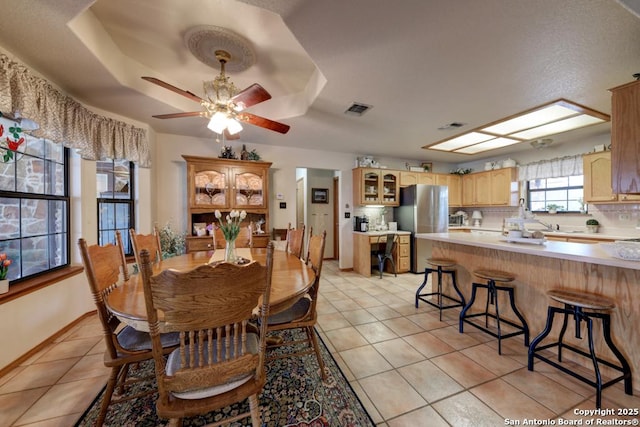 dining room featuring visible vents, ceiling fan, baseboards, light tile patterned flooring, and a raised ceiling