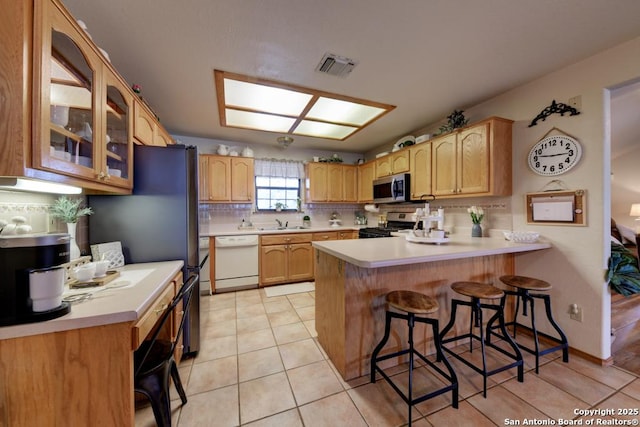 kitchen with glass insert cabinets, a breakfast bar, decorative backsplash, a peninsula, and stainless steel appliances