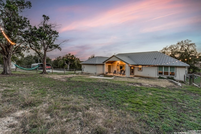 back of property at dusk with a gate, a patio, fence, a yard, and metal roof