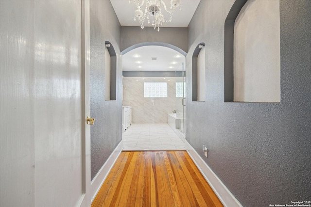 corridor with arched walkways, wood finished floors, baseboards, and a textured wall