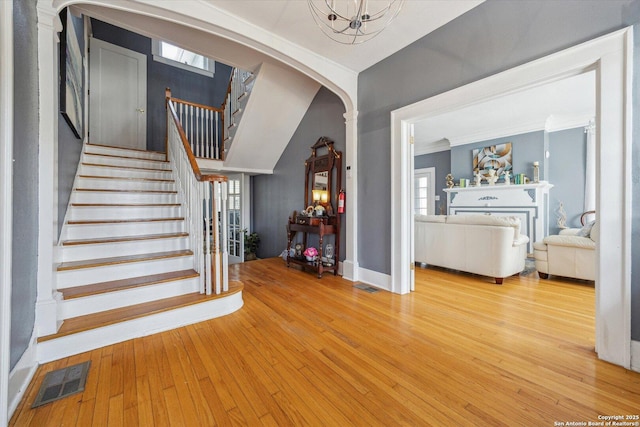 staircase with visible vents, arched walkways, ornamental molding, and hardwood / wood-style flooring