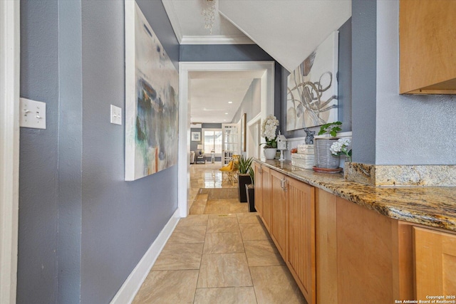 corridor featuring light tile patterned floors, a textured wall, baseboards, and ornamental molding