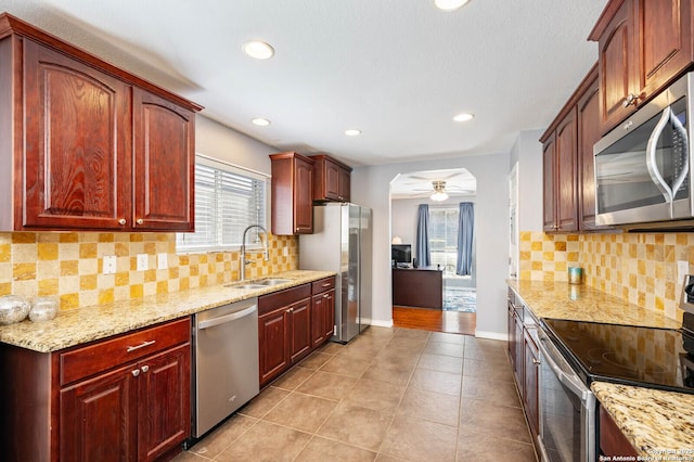 kitchen with light stone countertops, ceiling fan, a sink, appliances with stainless steel finishes, and reddish brown cabinets