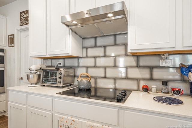 kitchen with range hood, white cabinetry, light countertops, and black electric cooktop