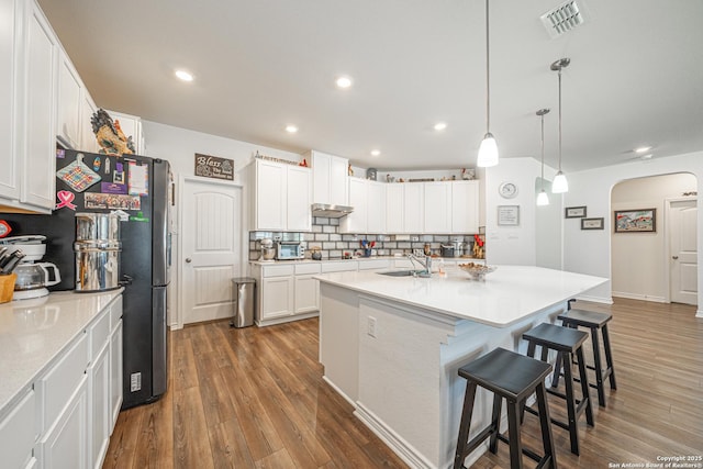 kitchen featuring arched walkways, visible vents, a kitchen breakfast bar, and wood finished floors