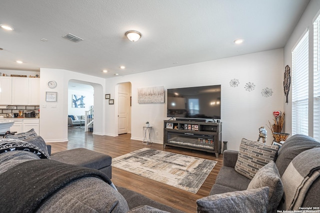 living area featuring arched walkways, visible vents, recessed lighting, and wood finished floors