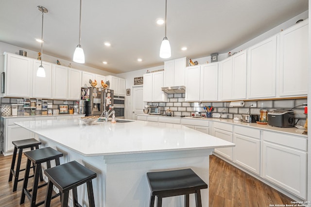 kitchen with tasteful backsplash, dark wood-type flooring, a kitchen bar, appliances with stainless steel finishes, and a kitchen island with sink