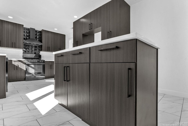 kitchen featuring light countertops, marble finish floor, gas range oven, and wall chimney range hood