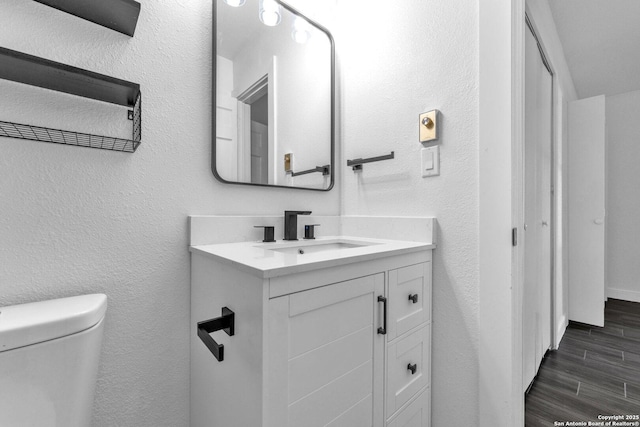 bathroom featuring a textured wall, vanity, wood tiled floor, and toilet