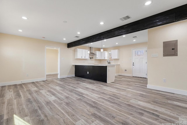 kitchen featuring visible vents, beam ceiling, electric panel, light countertops, and wall chimney exhaust hood