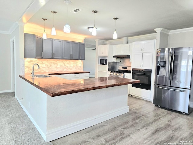 kitchen featuring a sink, wood counters, backsplash, stainless steel appliances, and a peninsula