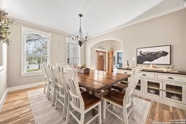 dining area with an inviting chandelier, light wood-style flooring, arched walkways, and ornamental molding