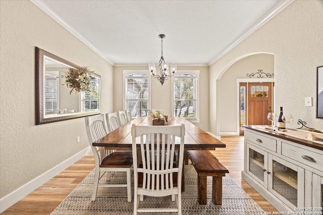 dining room with baseboards, light wood-type flooring, ornamental molding, an inviting chandelier, and a textured wall