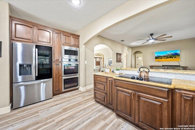 kitchen with light stone counters, brown cabinets, stainless steel appliances, light wood-style floors, and a textured ceiling