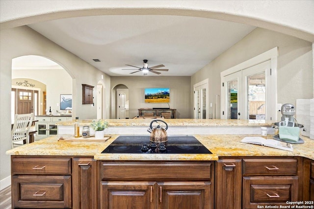 kitchen featuring visible vents, a ceiling fan, open floor plan, black electric stovetop, and light stone countertops