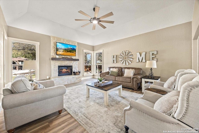 living area featuring a stone fireplace, ceiling fan, wood finished floors, and a healthy amount of sunlight