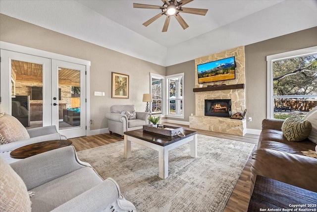 living area with baseboards, french doors, a fireplace, wood finished floors, and a ceiling fan