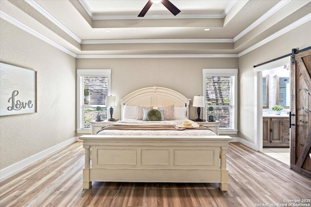 bedroom with a tray ceiling, a barn door, crown molding, and light wood finished floors