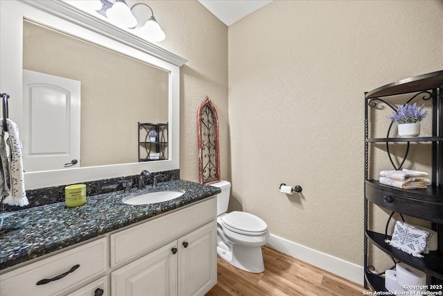 half bath featuring baseboards, toilet, wood finished floors, a textured wall, and vanity