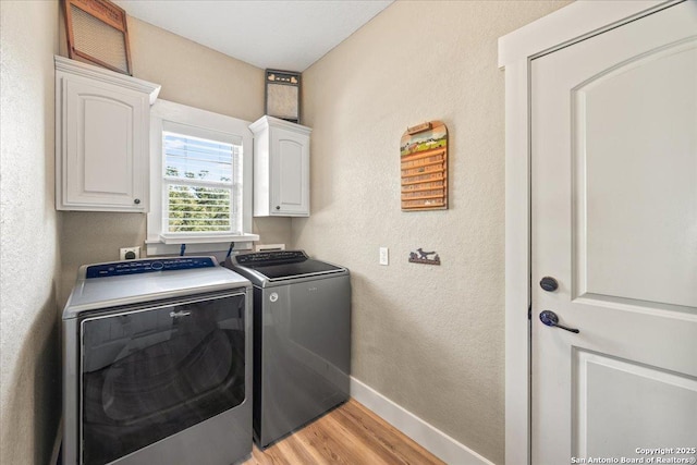 laundry area with washing machine and clothes dryer, light wood finished floors, baseboards, a textured wall, and cabinet space