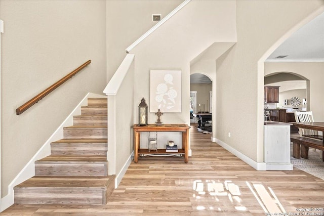 stairs with visible vents, wood finished floors, arched walkways, a high ceiling, and baseboards