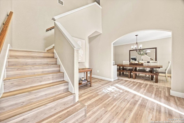 staircase with wood finished floors, visible vents, baseboards, arched walkways, and a chandelier