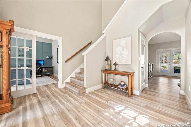 foyer entrance with stairway, baseboards, light wood-style flooring, arched walkways, and french doors