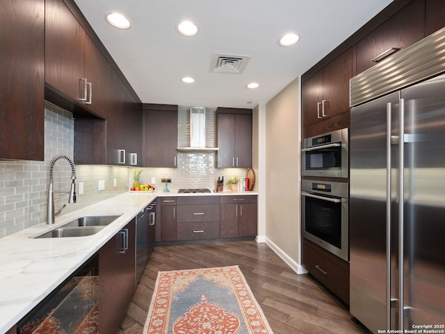 kitchen with visible vents, dark wood finished floors, a sink, stainless steel appliances, and wall chimney range hood