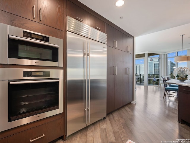 kitchen featuring dark brown cabinetry, a wall of windows, recessed lighting, light wood-style flooring, and stainless steel appliances