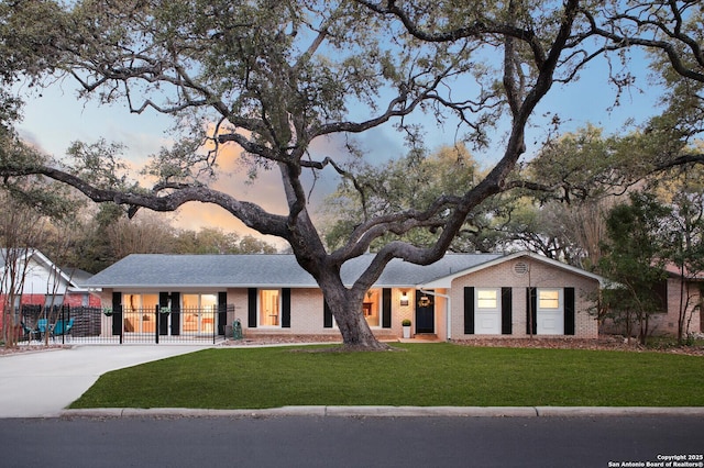 view of front of property featuring brick siding, a lawn, concrete driveway, and fence