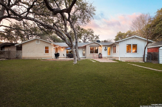 rear view of house with a lawn, fence, board and batten siding, brick siding, and a patio area