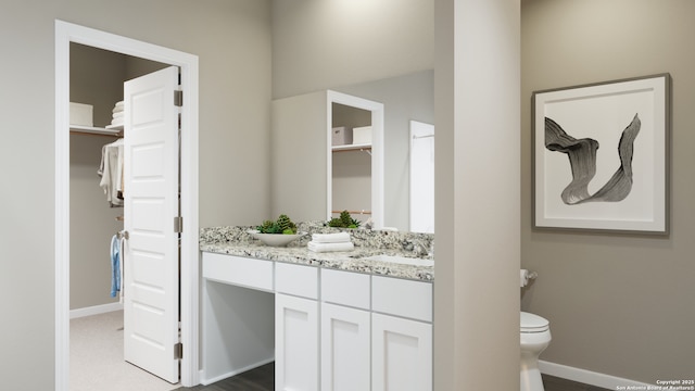 full bathroom with a walk in closet, toilet, a sink, double vanity, and baseboards