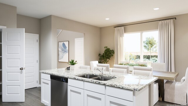 kitchen featuring a center island with sink, a sink, stainless steel dishwasher, white cabinetry, and light stone countertops