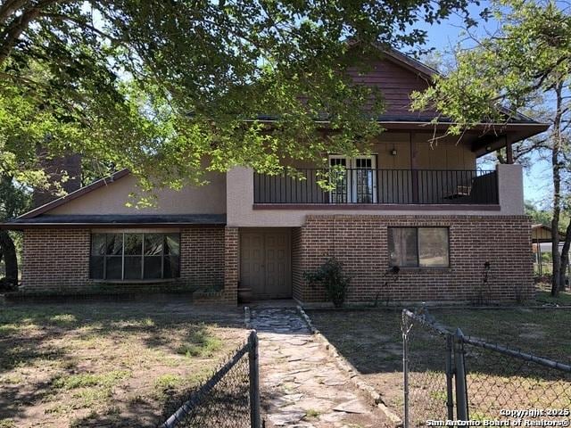 view of front of house featuring a balcony, fence, and brick siding