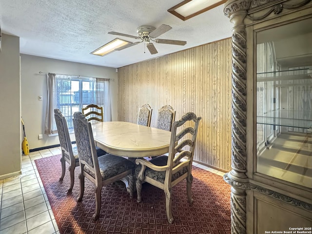 tiled dining space featuring baseboards, wood walls, a textured ceiling, and ceiling fan