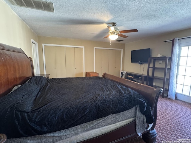 carpeted bedroom featuring visible vents, a textured ceiling, two closets, and a ceiling fan