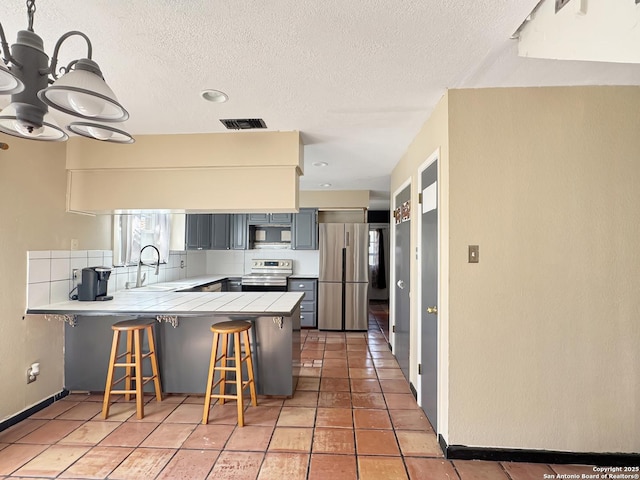 kitchen with visible vents, a peninsula, a kitchen breakfast bar, stainless steel appliances, and a sink