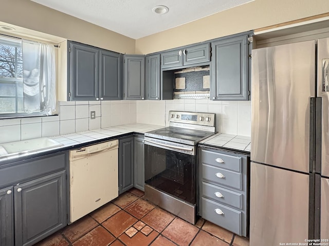 kitchen with tile countertops, gray cabinetry, and stainless steel appliances